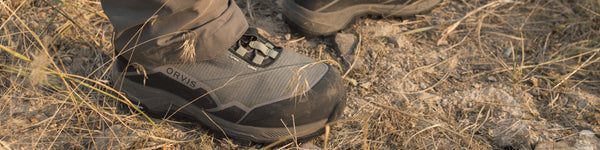 A wading boot balances on rounded rocks in a shallow stream