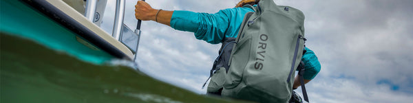 A bearded angler wearing a backpack casts their line.