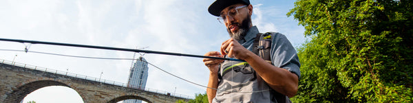 An angler wading in an urban river focuses on tying their line.