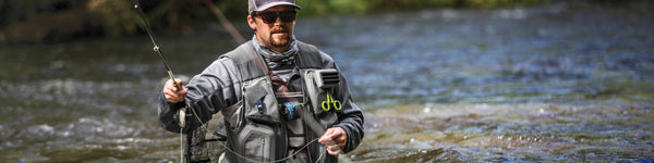 An angler with tools hanging from their fishing vest wades wait-deep in the river.