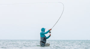 An angler casts, wading waist-deep in the ocean