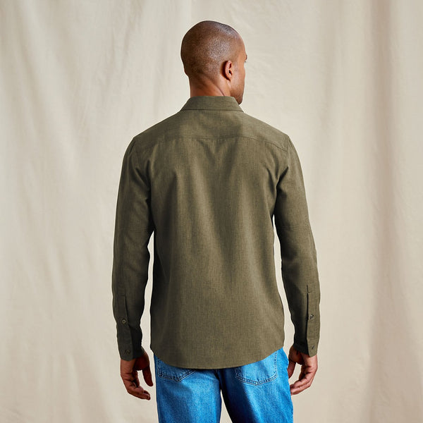 Man wearing a green shirt and blue jeans against a beige background