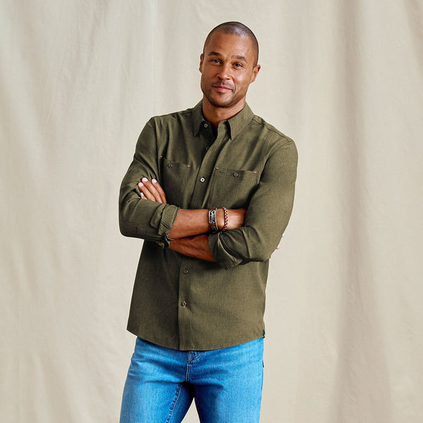 Man wearing an olive green shirt and blue jeans against a beige background
