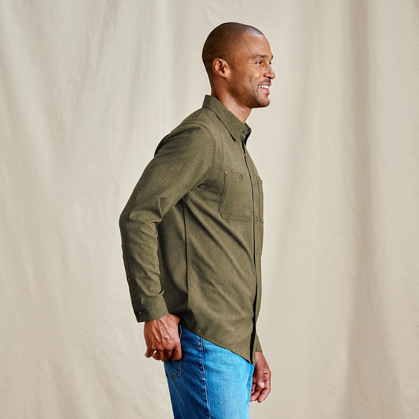 Man wearing a green jacket and blue jeans against a beige background