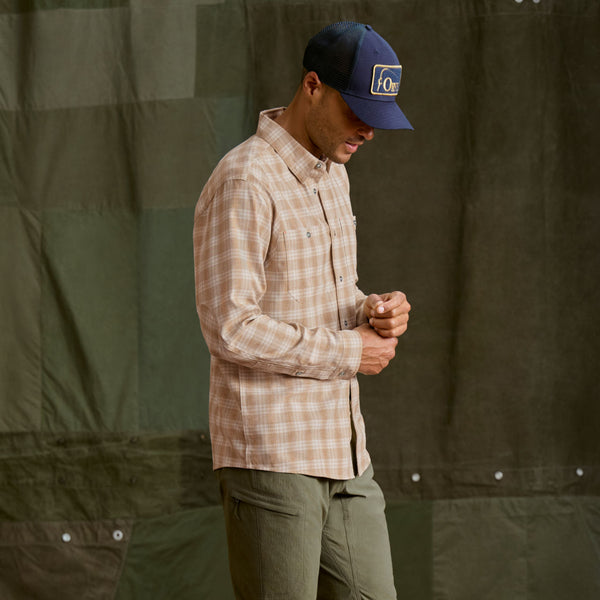 Man wearing dark green trousers, beige checkered shirt and dark blue cap