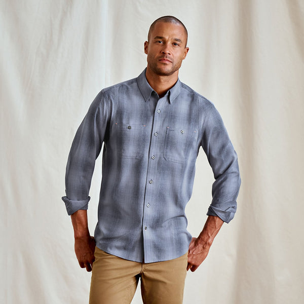 Man wearing a blue checkered shirt and beige pants against a plain background