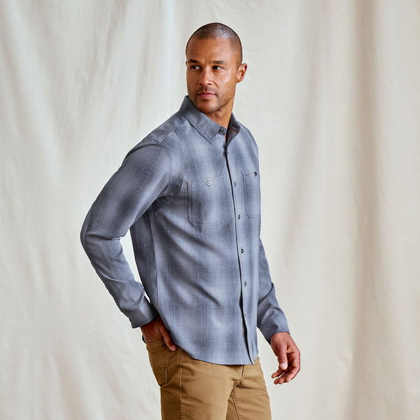 Man wearing a blue checkered shirt and brown pants against a plain background