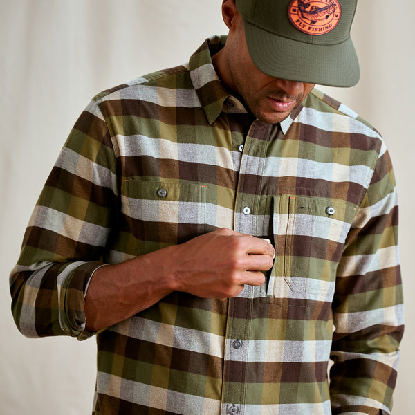 Person wearing a plaid shirt and cap with a logo, against a neutral background
