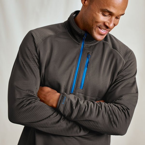 Man wearing a gray pullover with a blue zipper on a plain background