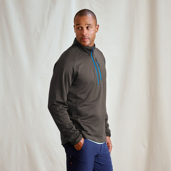 Man wearing a gray pullover with a blue zipper against a plain background
