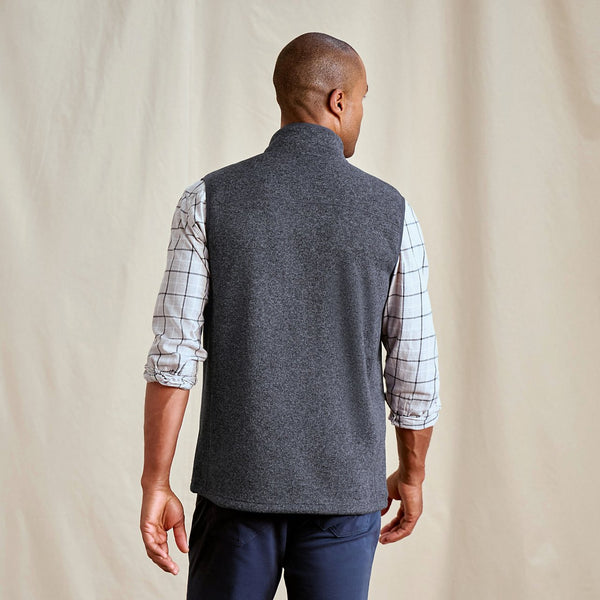 Man wearing a grey vest over a plaid shirt against a beige background