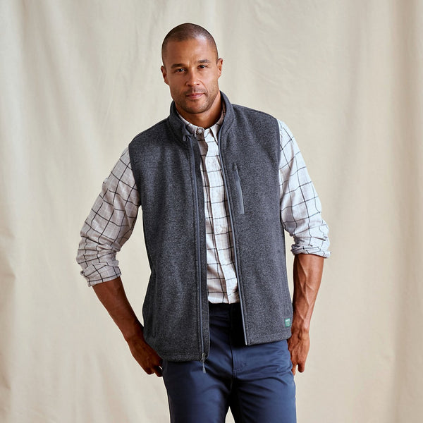 Man wearing a grey vest over a plaid shirt with a beige background