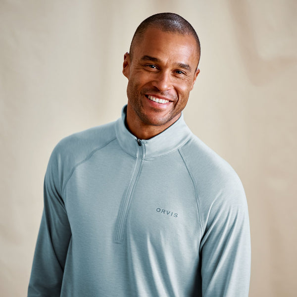 Man wearing a light blue Orvis pullover against a beige background