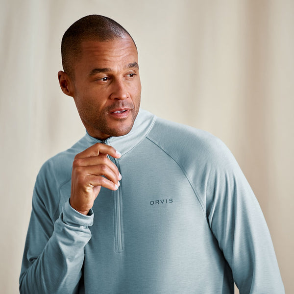 Man wearing a light blue pullover with 'Orvis' logo, standing against a neutral background