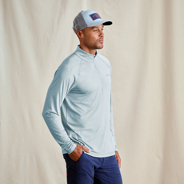 Man wearing a light blue long-sleeve shirt and dark blue pants against a beige background