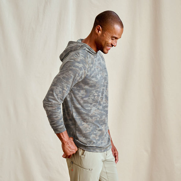 Man wearing a gray camouflage hoodie and beige pants against a plain background