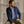 Load image into Gallery viewer, Man wearing a navy jacket over a checkered shirt sitting against a stone wall.