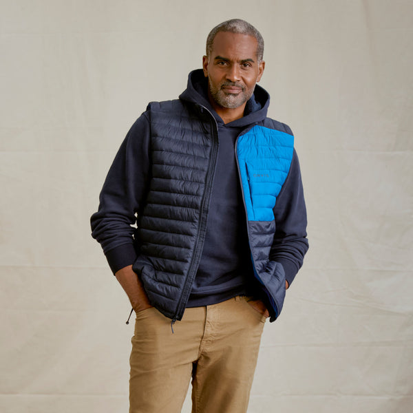 man wearing dark blue hoodie, blue gilet and beige pants