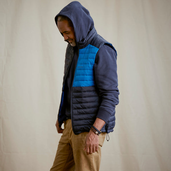 man wearing dark blue hoodie and blue gilet, beige pants