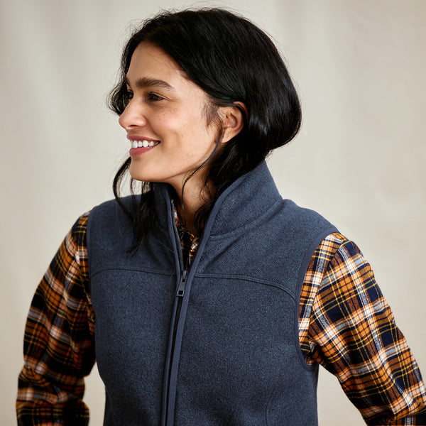 Woman wearing a blue vest over a plaid shirt against a neutral background