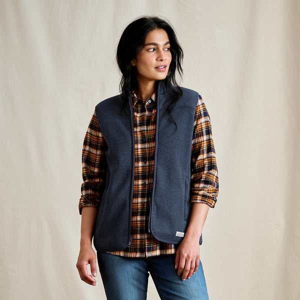 Woman wearing a blue vest over a plaid shirt on a beige background