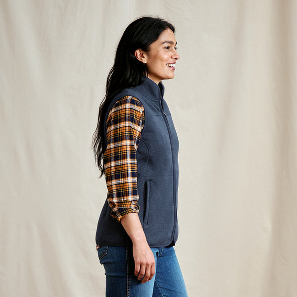 Woman wearing a blue vest over a plaid shirt with a beige background