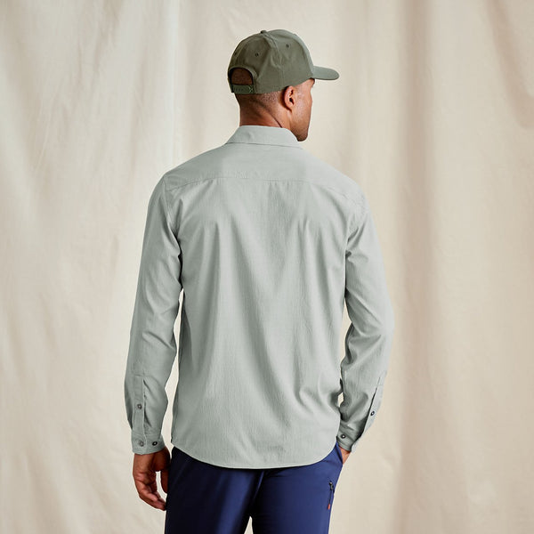 Man wearing a light grey long-sleeve shirt and blue pants against a beige background