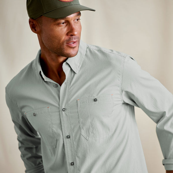 Man wearing a light grey shirt and green cap against a beige background