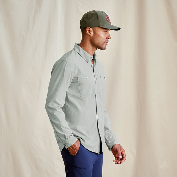 Man wearing a light grey shirt and green cap against a beige background