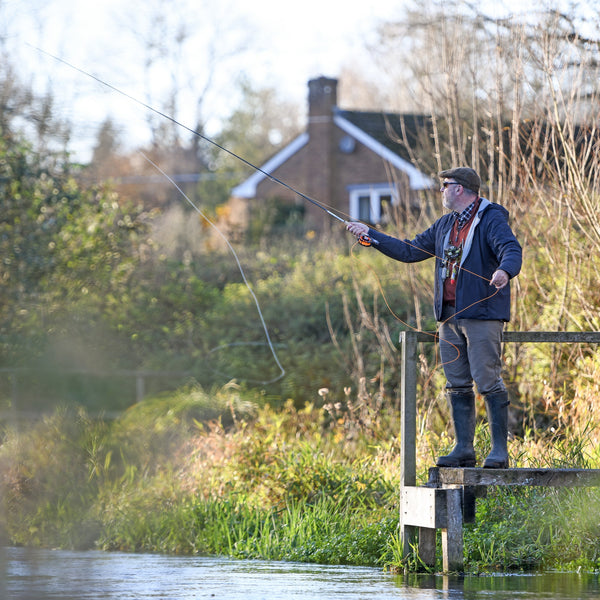 A person fly fishing in a river, standing on a wooden platform