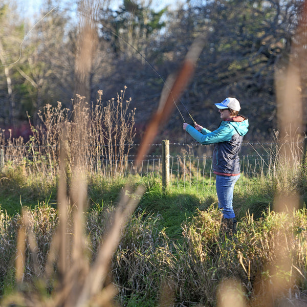 man fly fishing from the side of the river
