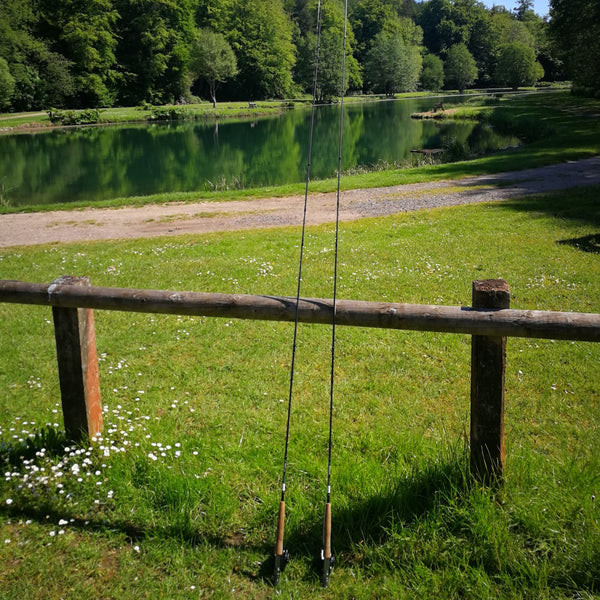 two fly rods leaning on wooden fence in front of river