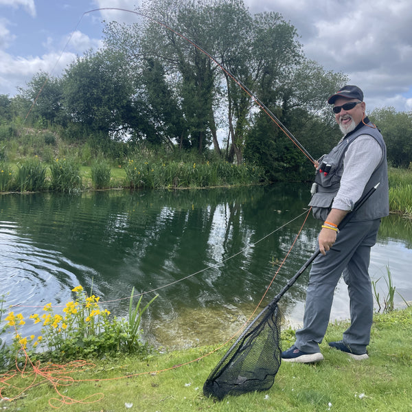 Man fishing by a lake with trees and grass in the background