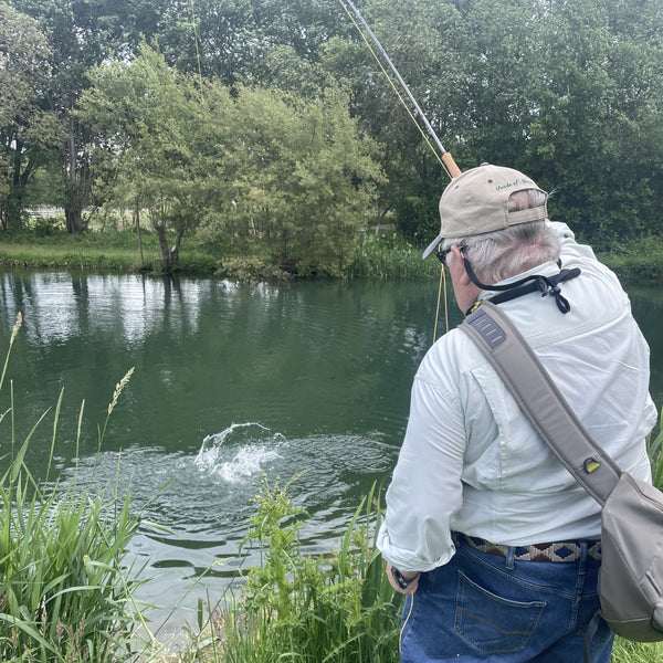 Man fishing by a pond with trees in the background