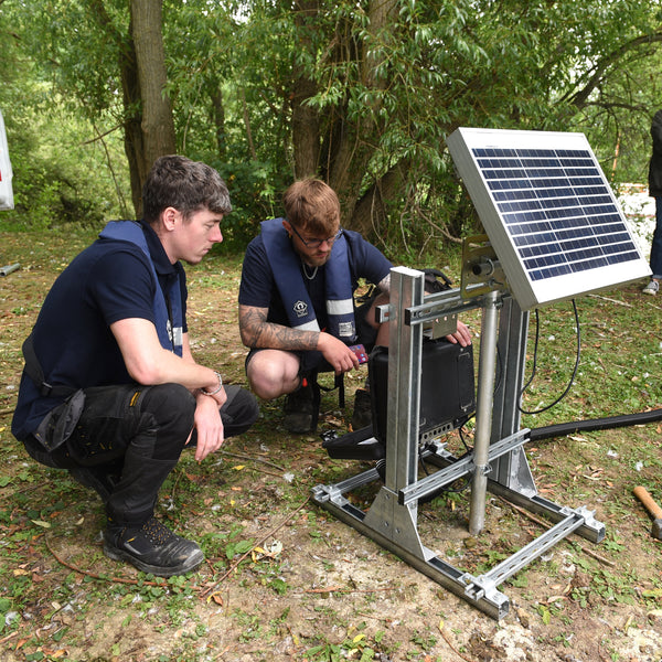 Two people working on a piece of equipment with a solar panel outdoors.