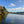 Load image into Gallery viewer, A scenic view of a river with trees on the bank under a blue sky with clouds.