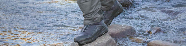 A wading boot balances on rounded rocks in a shallow stream