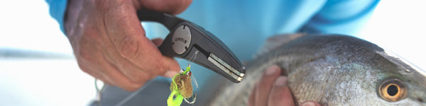 An angler holds a pair of pliers in one hand and a fresh catch in the other.