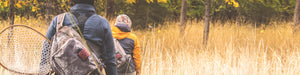 Rear-view of two anglers wearing backpacks and heading into the woods