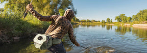 An angler wearing a camo hoodie nets a fish out of the river