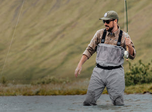 man wading in water wearing green cap and grey waders