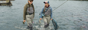Two woman walking in river waering waders and holding fly rods and fishing net