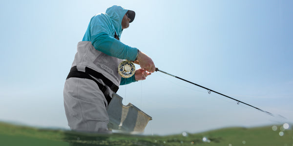 man fly fishing in water wearing grey waders and blue hoodie