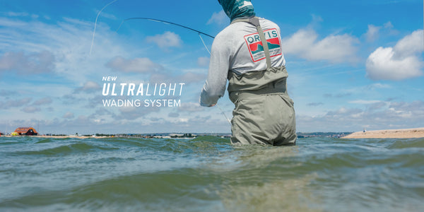 Person fishing in water wearing a waders with 'Orvis' branding, under a blue sky.