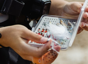 Person holding a container of fishing flies with a close-up of a fly.