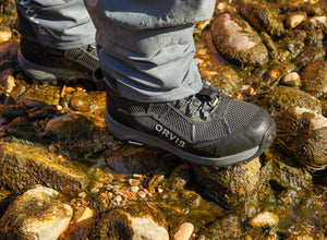 Person wearing Orvis wading boots on a rocky stream bed