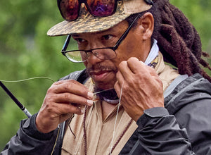 A dreadlocked gentleman wearing glasses fine-tunes his line