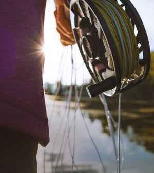 Fishing reel held by a person with a blurred lake and trees in the background