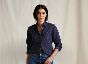 Woman wearing a dark blue patterned shirt and jeans against a plain background