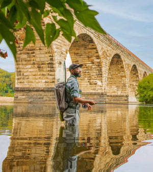 An angler wades in the river beneath a bridge of stone arches
